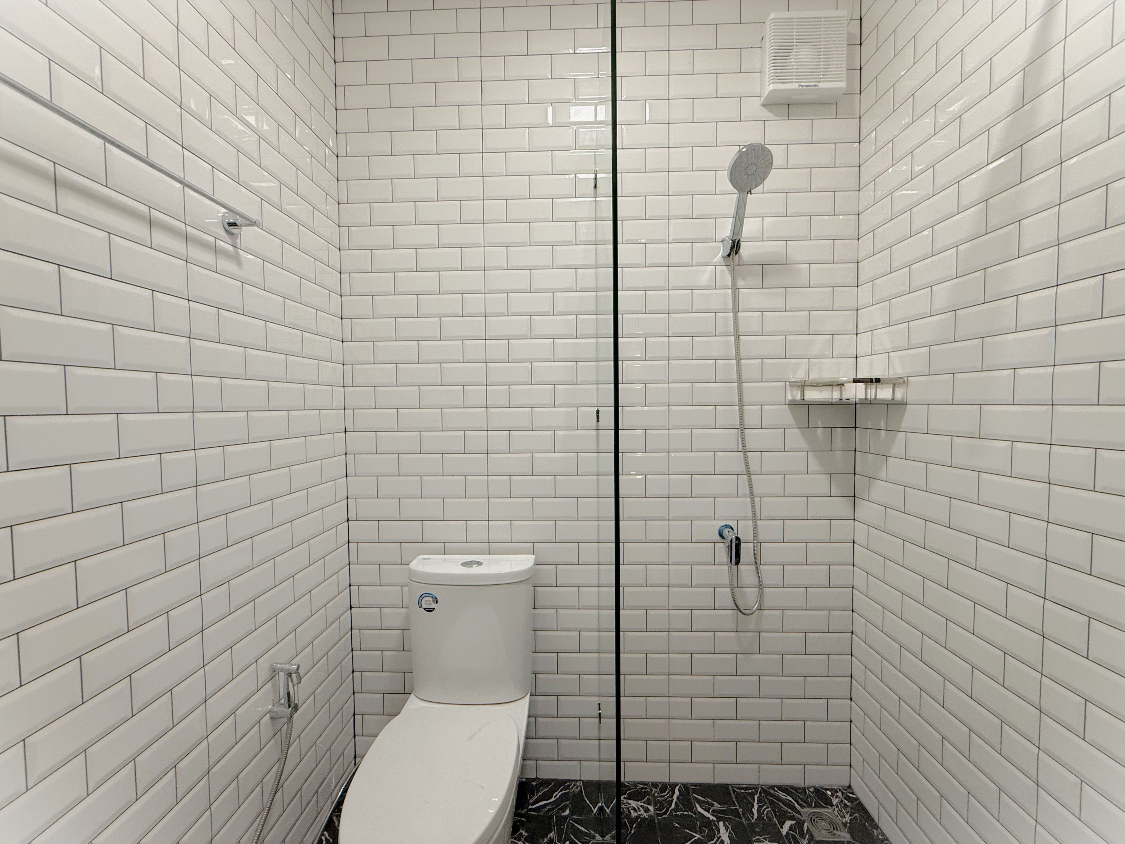 A bathroom with white subway tiles, a toilet, a shower with a handheld showerhead, and a towel rack.
