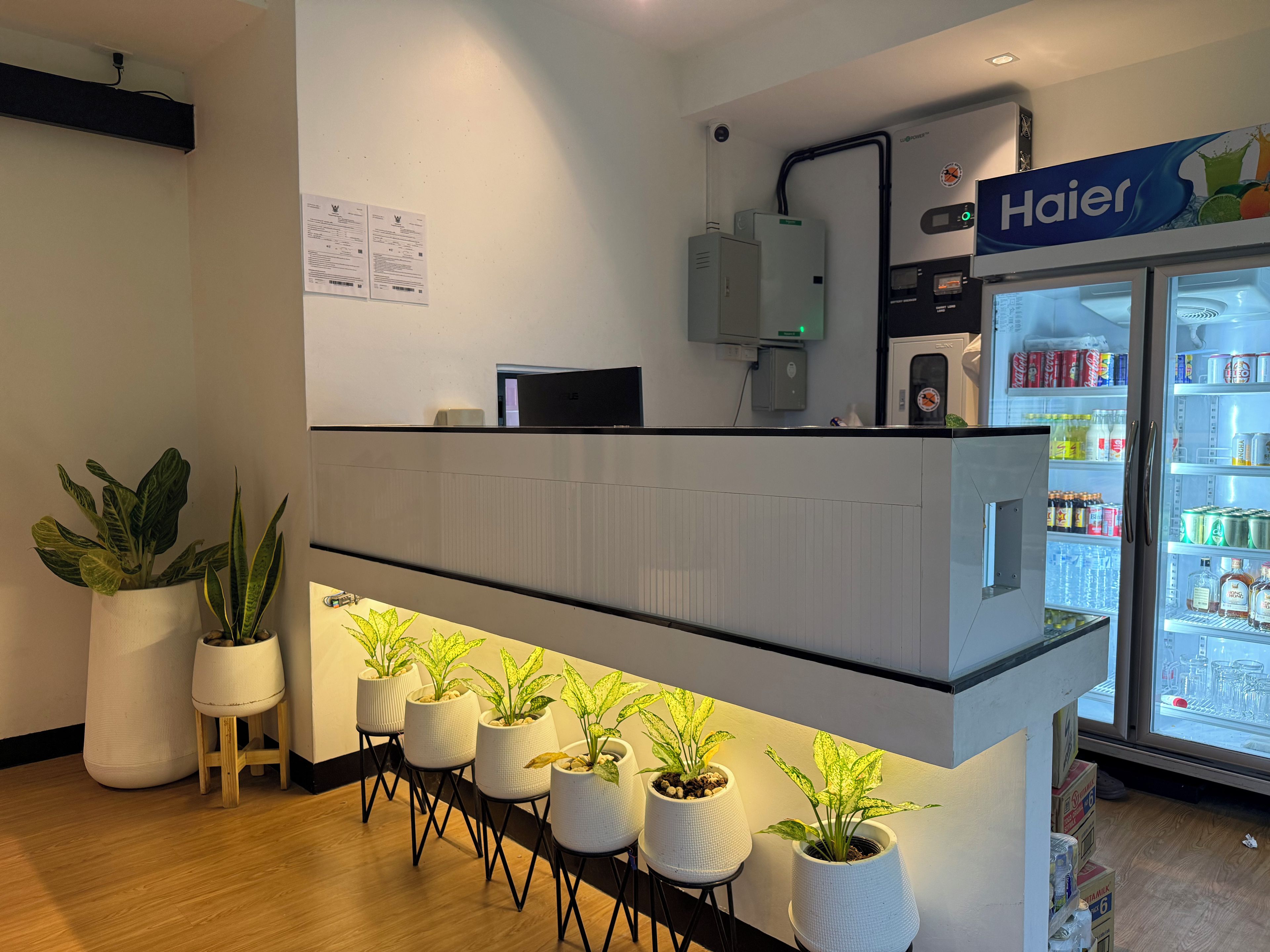 A reception desk with a Haier refrigerator stocked with beverages, a computer, and a wall-mounted security camera.