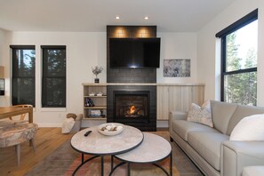 A modern living room with a fireplace, a flat-screen TV, and a sofa. - Luxe Bridger Bowl Chalet (Bozeman)