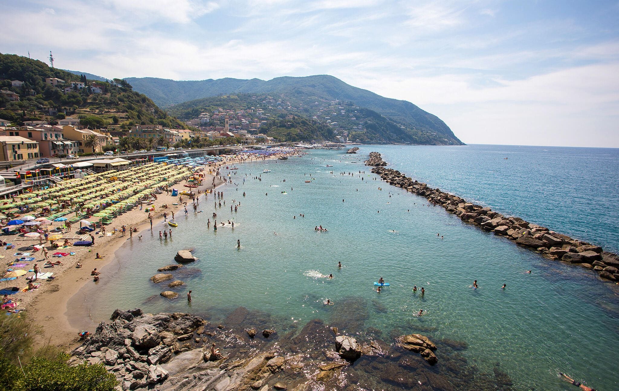 A coastal beach with clear waters, rocky shoreline, and a row of beach umbrellas.