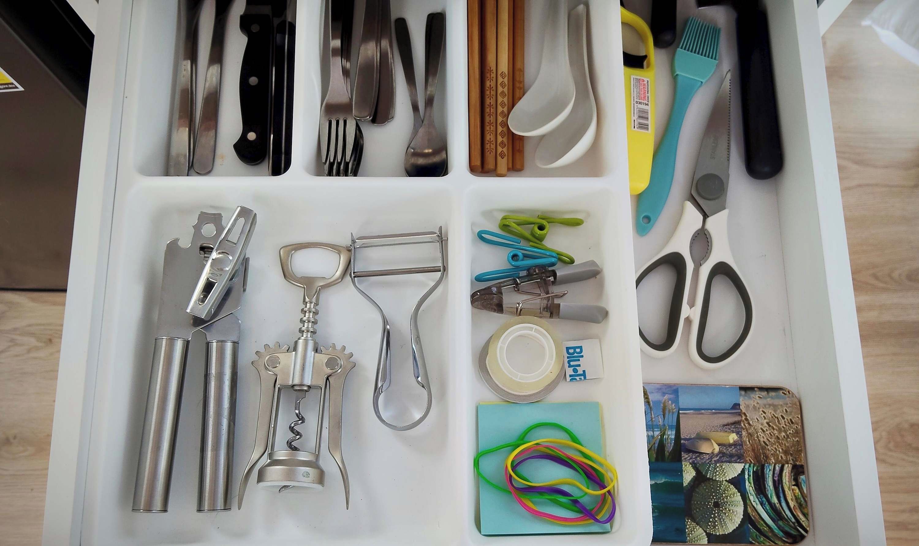 A drawer containing various kitchen utensils, including knives, forks, spoons, and a corkscrew.