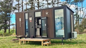 A modern cabin with a large sliding door, a small kitchen area, and a deck with outdoor seating.