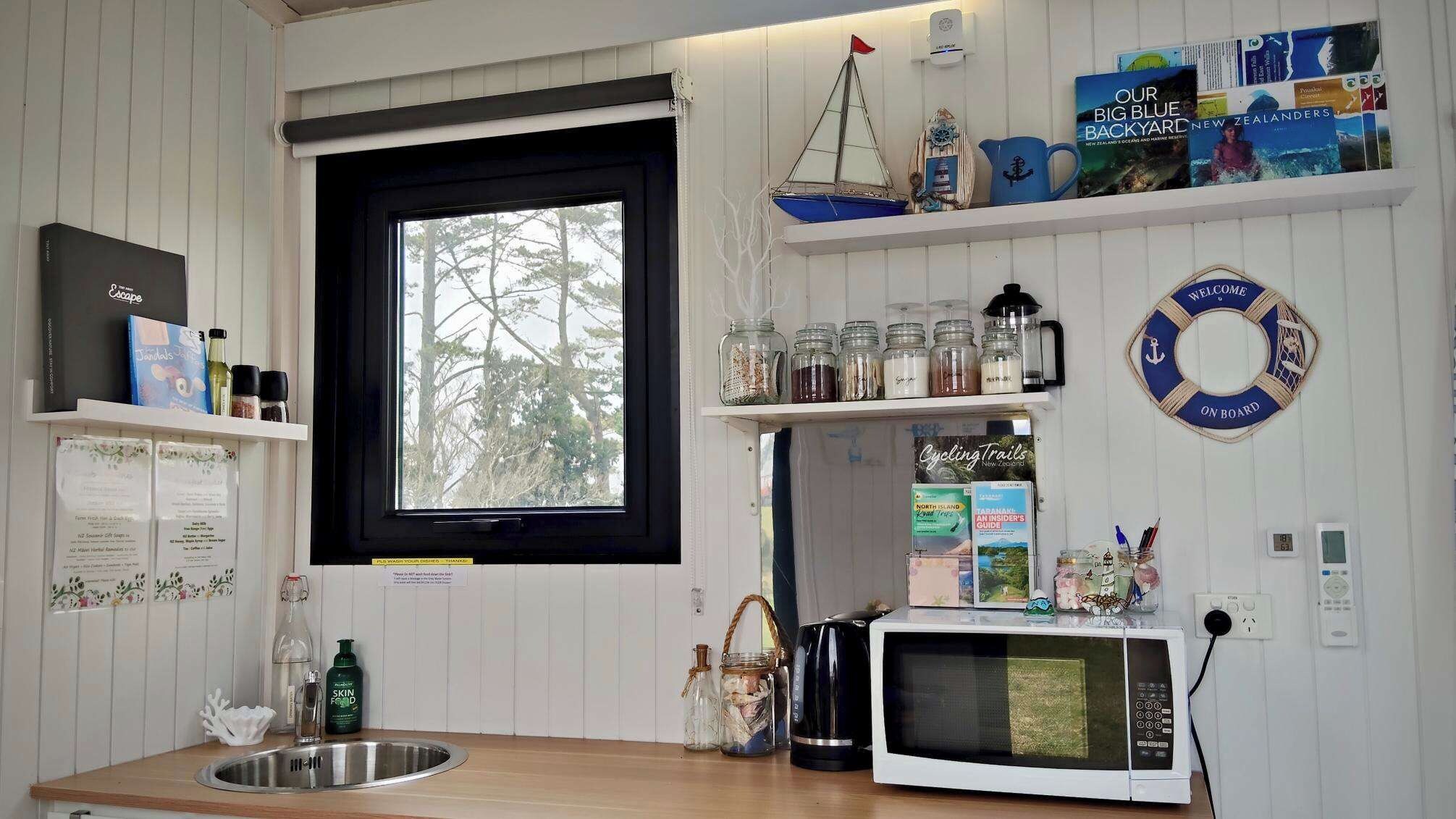 A kitchen with a window, shelves with books, a kettle, and a microwave.