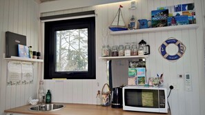 Una cocina con ventana, estantes con libros, un hervidor y un microondas.