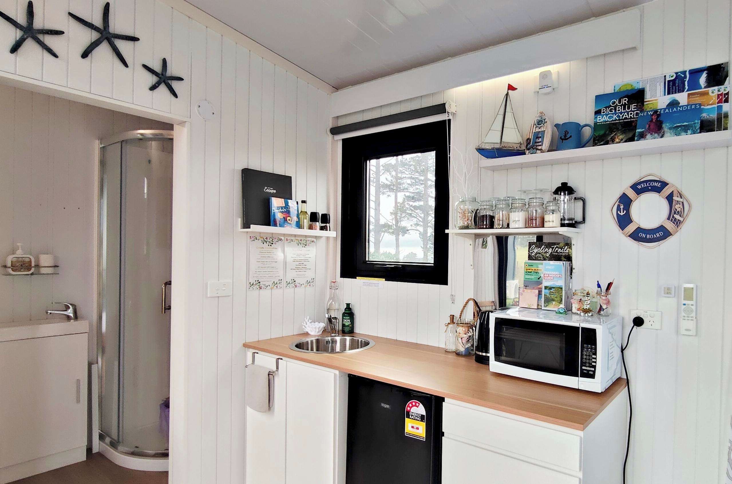 A compact kitchen with a sink, microwave, and a window. There are shelves with various items and a life ring decoration.