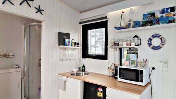 A compact kitchen with a sink, microwave, and a window. There are shelves with various items and a life ring decoration.