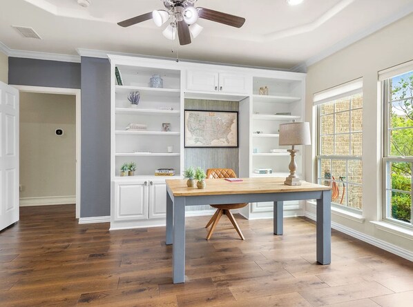 Une pièce spacieuse comprenant une table à manger, des étagères intégrées et un ventilateur de plafond.