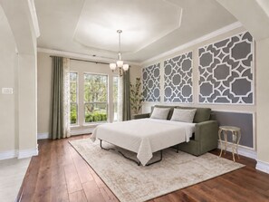 Ein Schlafzimmer mit einem großen Bett, einem grünen Sofa, einem kleinen Tisch und einer dekorativen Wandverkleidung.