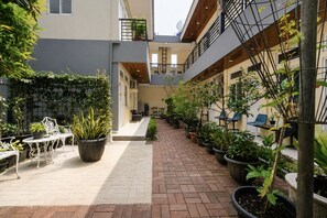 A courtyard with potted plants, outdoor seating, and a brick pathway. - Collection O near Club Golf Bogor Raya (Bogor)