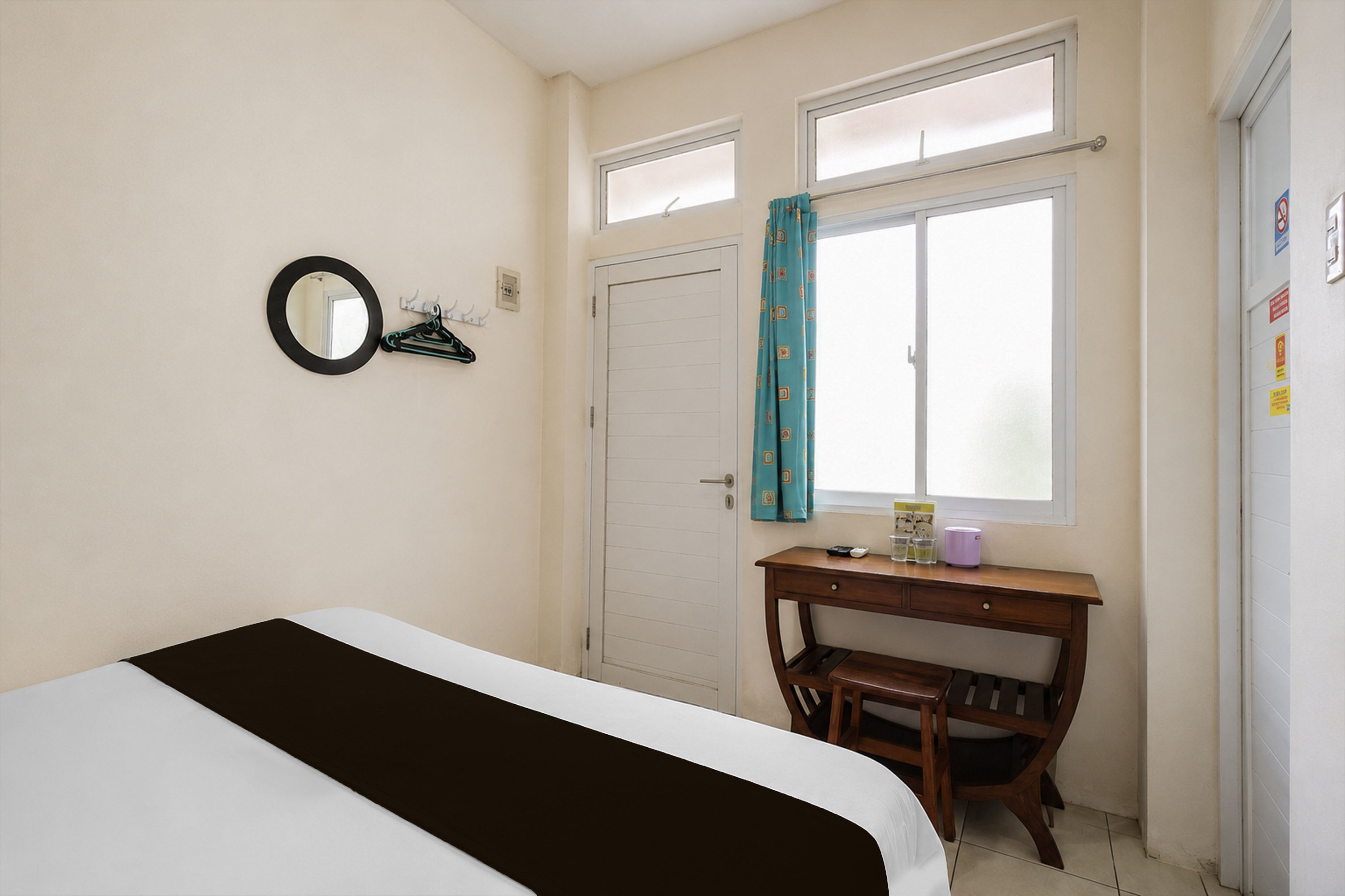 Un dormitorio con cama, escritorio, silla, ventana con cortinas y puerta.