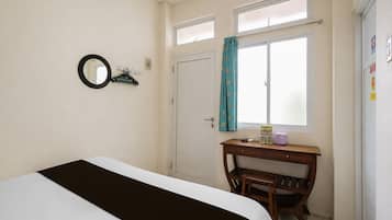Un dormitorio con cama, escritorio, silla, ventana con cortinas y puerta.