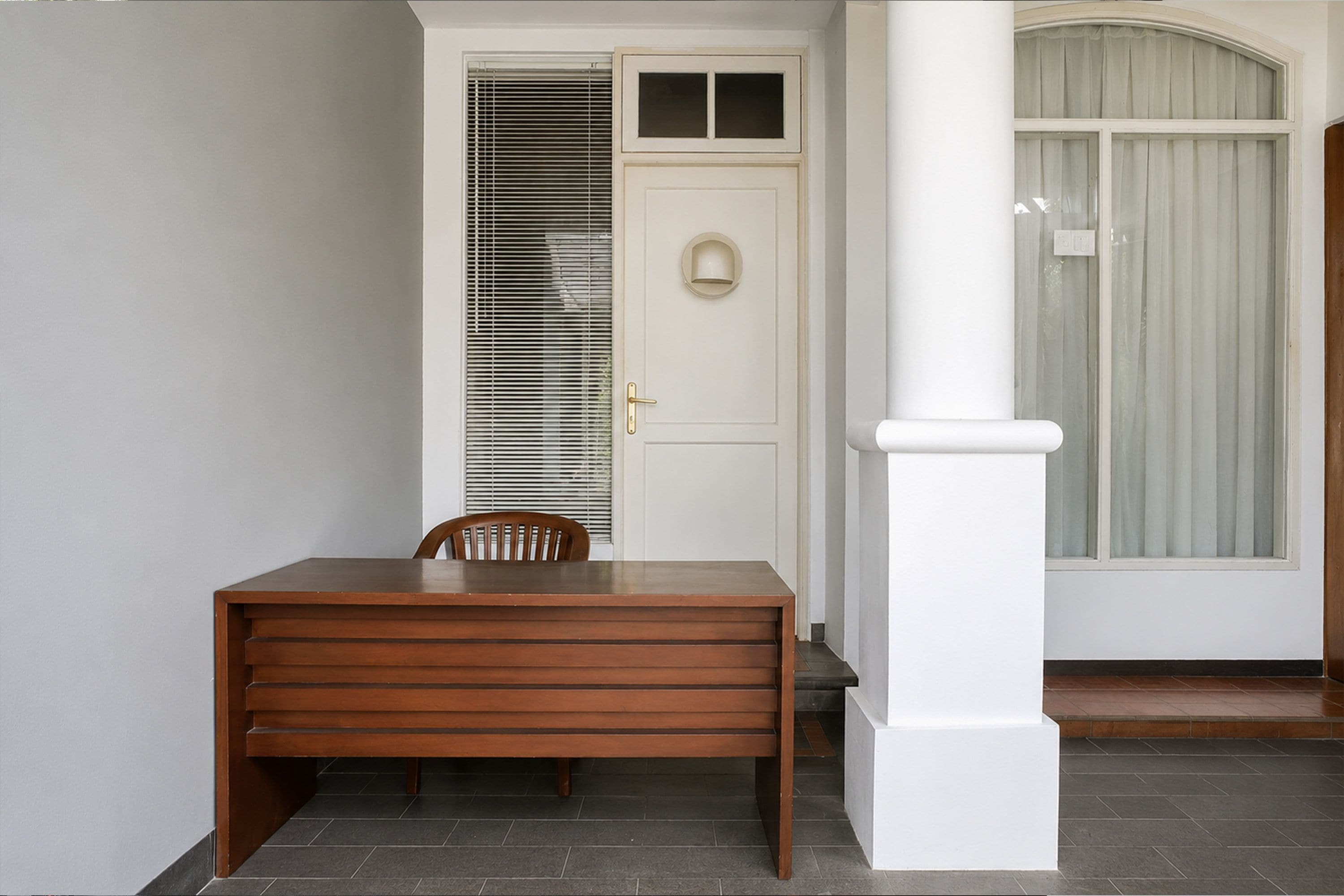 Una mesa de madera con una silla, una puerta blanca con un ventanal y un pilar blanco.
