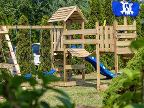 A wooden playground structure with slides and climbing elements, surrounded by greenery. - Sommerhaus Albatros II by Interhome (Rewal)