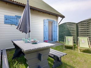 A wooden outdoor table with benches, a blue umbrella, and a green chair with a website banner. - Sommerhaus Albatros II by Interhome (Rewal)