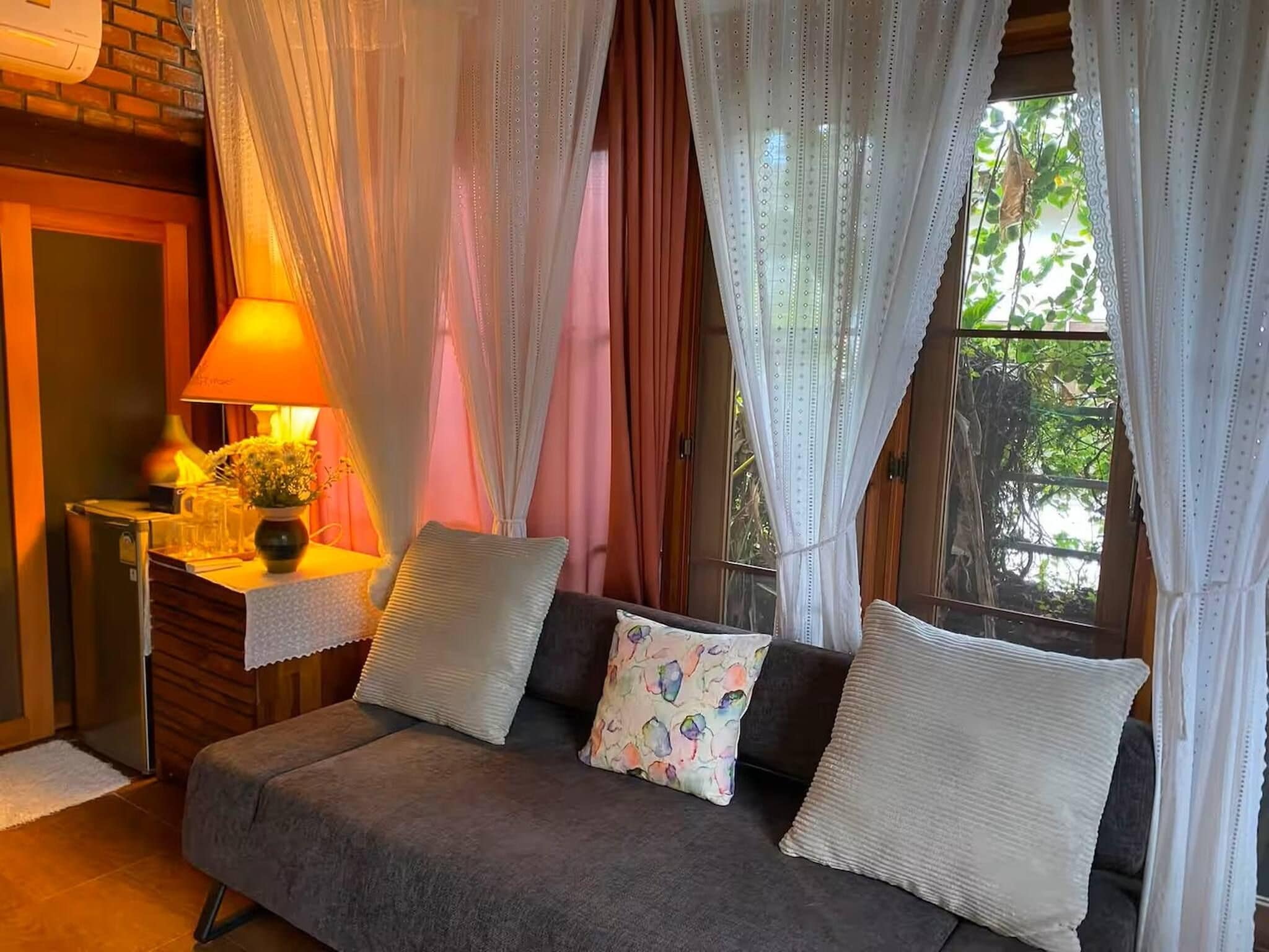 A cozy room with a sofa, a lamp, and a window with curtains.