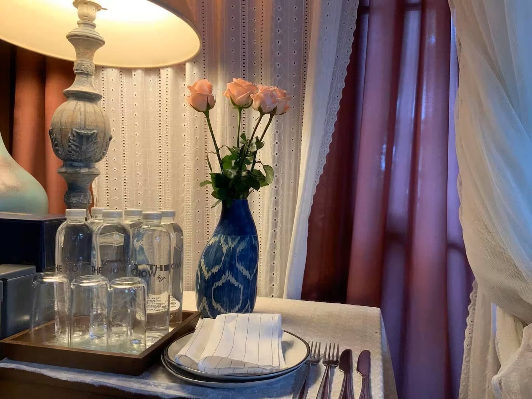 A table set with a blue vase, a tray with glasses, and a lit lamp.