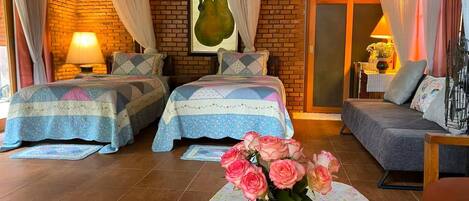 Habitación de hotel con dos camas, un sofá, una mesa con un florero y una pared de ladrillo.