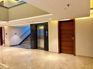 A modern interior with a marble floor, a wooden door, and a staircase leading to an upper level.