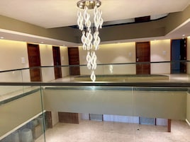 A hotel lobby with a glass railing, a central chandelier, and wooden doors.
