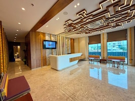 A hotel lobby with a reception desk, seating area, and large windows.