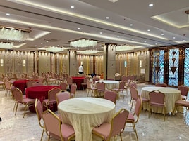 Un salón de banquetes con mesas y sillas redondas, una persona al fondo y paneles decorativos en la pared.