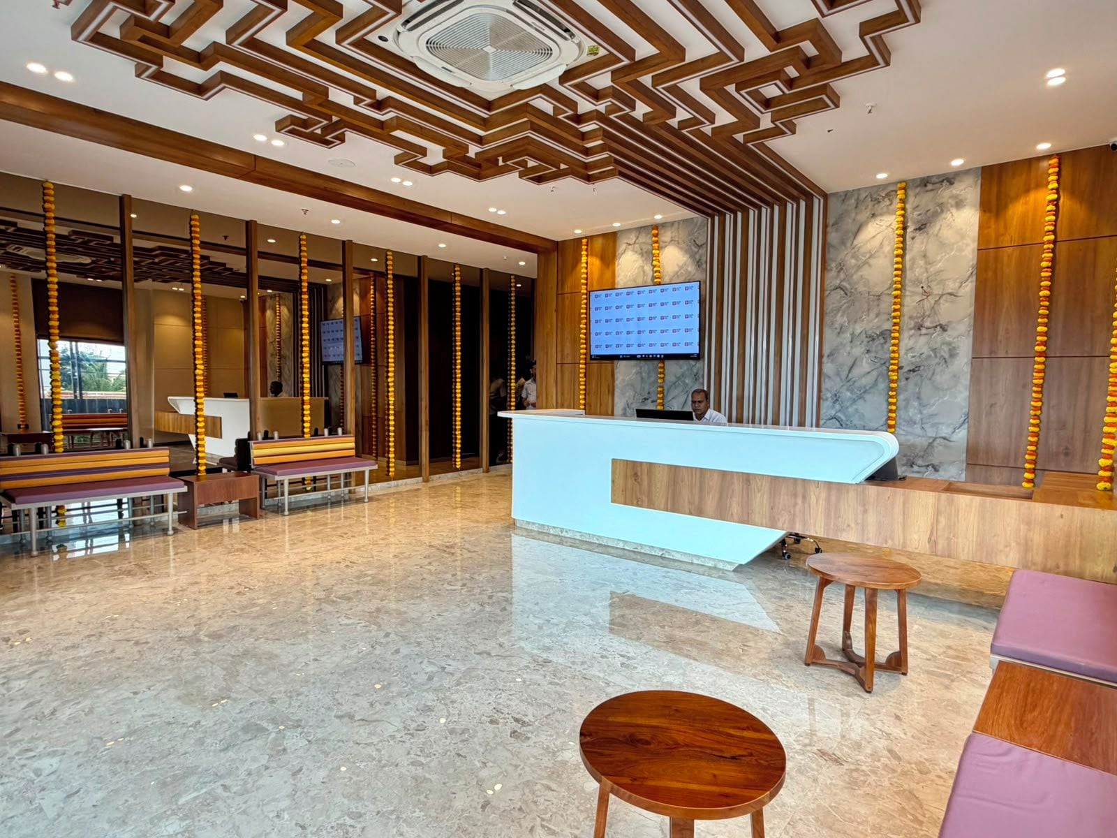 A hotel reception area with a modern design, featuring a reception desk, seating arrangements, and a large screen.
