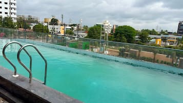 A swimming pool with a metal railing, surrounded by a fence, with buildings and trees in the background.