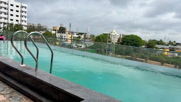 A swimming pool with a metal railing, a tiled deck, and a view of buildings in the background.