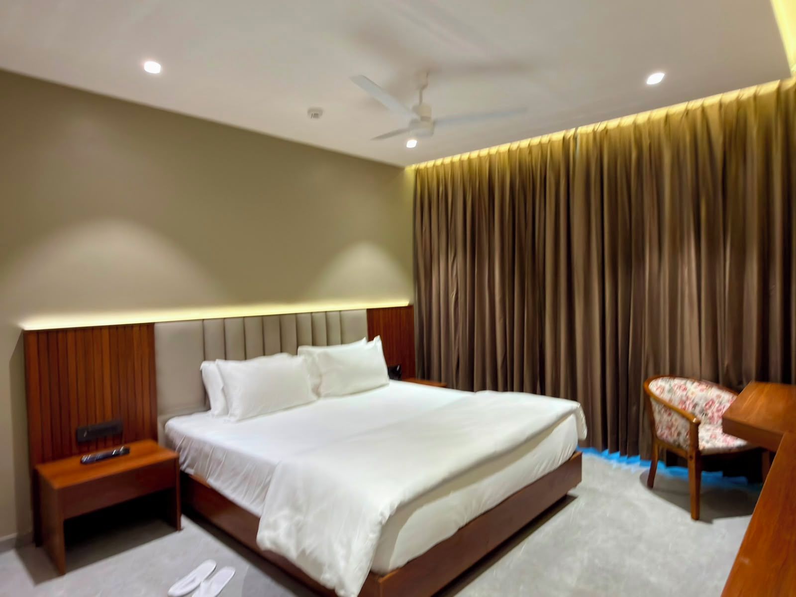 Une chambre d’hôtel moderne avec un grand lit, une table de chevet, une chaise et un ventilateur de plafond.