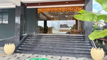 A modern building entrance with a staircase leading to a glass door, a decorative garland above the door, and a traditional rangoli design on the ground.