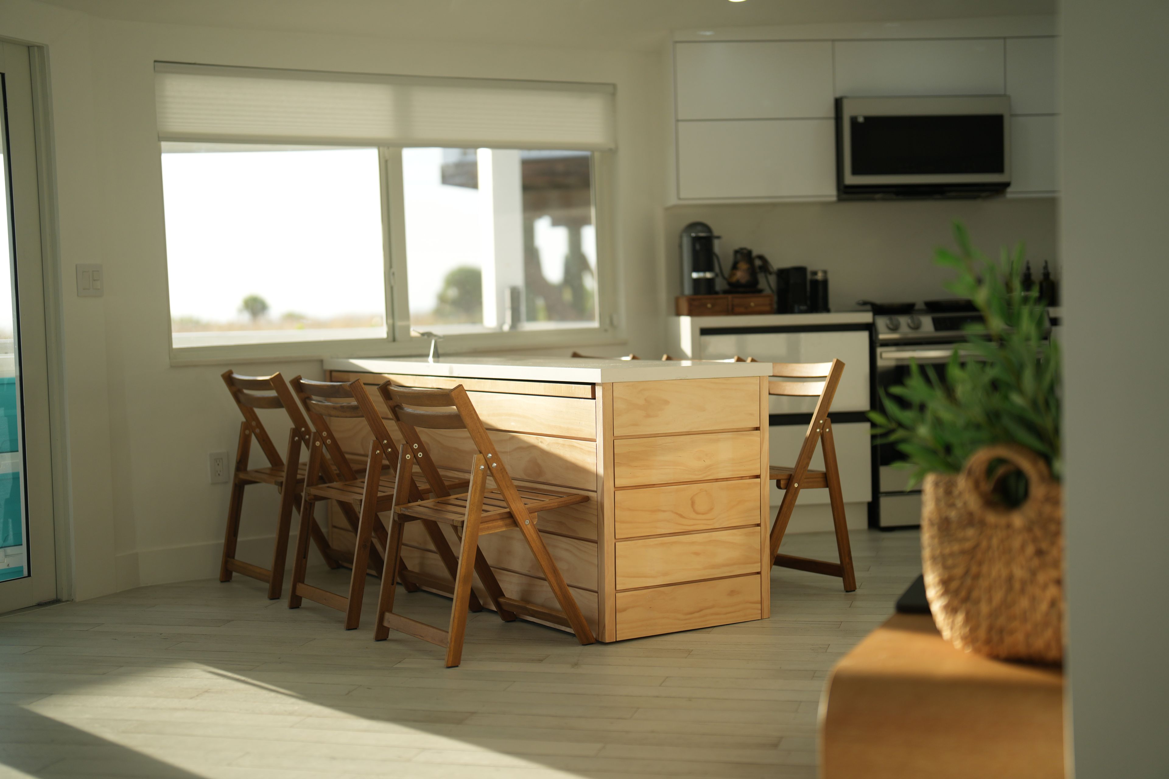 A modern kitchen with a central island, wooden chairs, and a large window.