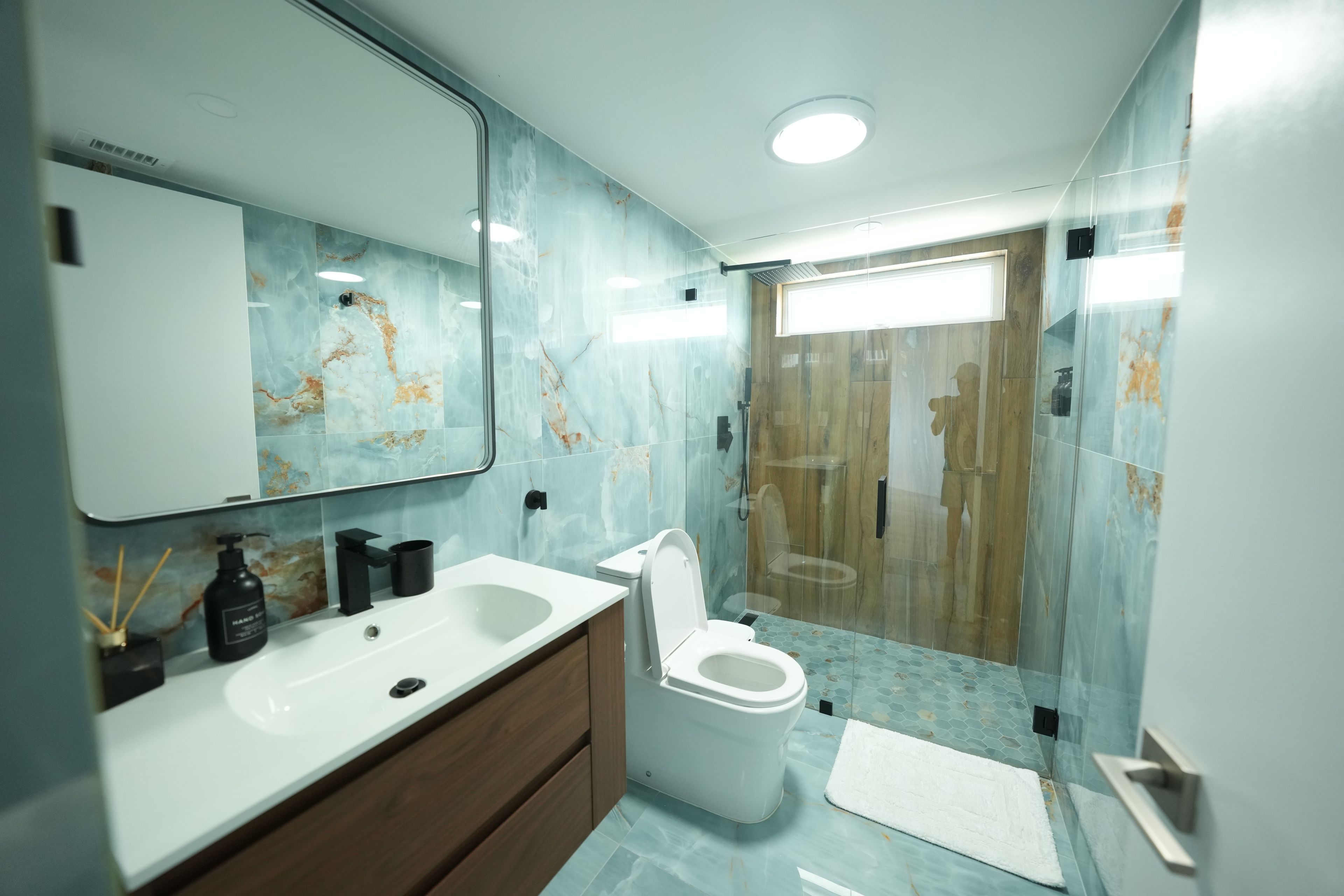 A modern bathroom with a large mirror, a sink, a toilet, and a shower area.