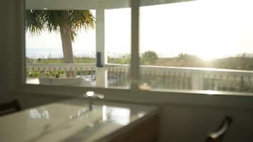 A room with a view of the ocean through a window, a bed, and a ceiling fan.