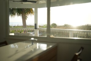 A room with a view of the ocean through a window, a bed, and a ceiling fan.