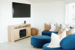 Una sala de estar moderna con un televisor de pantalla plana montado en la pared, un mueble de madera con espacio para el televisor y un sofá azul con varios cojines.