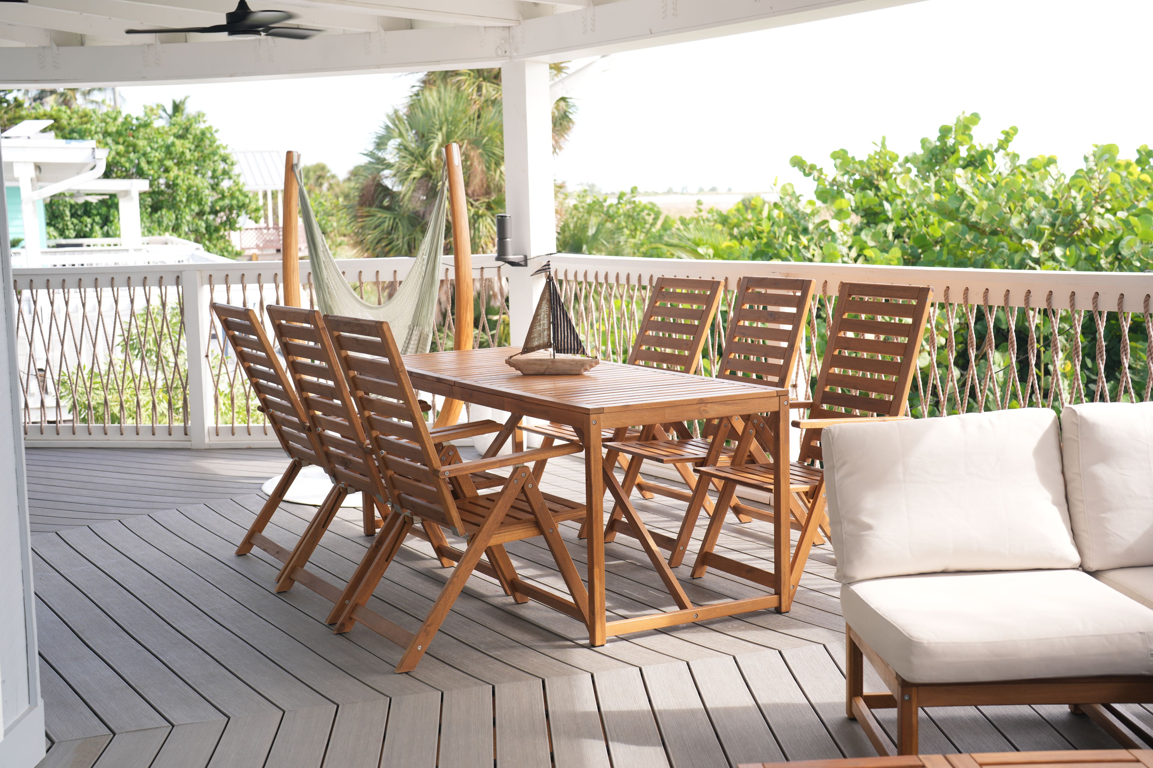 Um deck de madeira com mesa, cadeiras, uma rede e guarda-corpo branco.