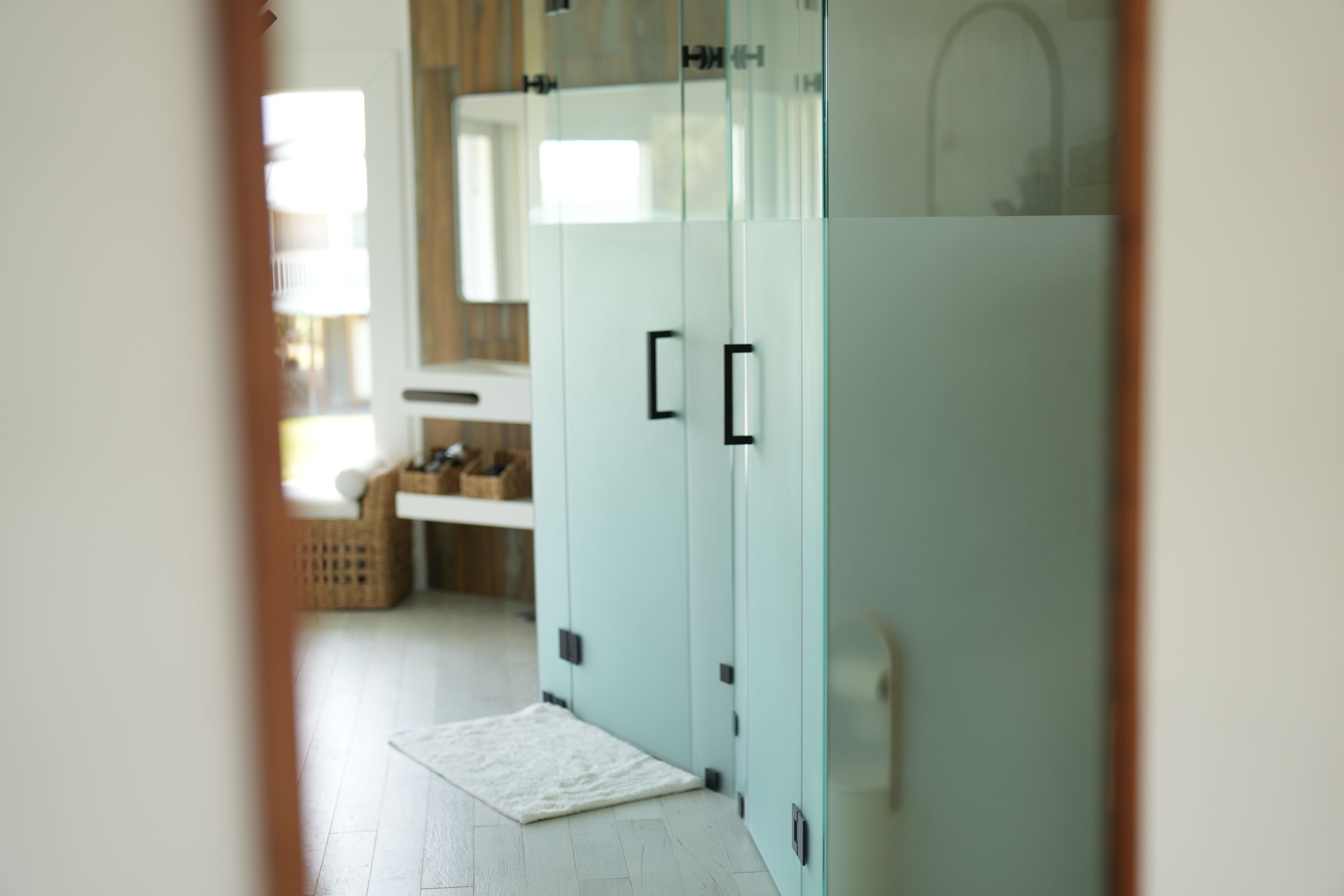 Une salle de bain moderne avec des portes en verre, un sol blanc et un petit tapis.