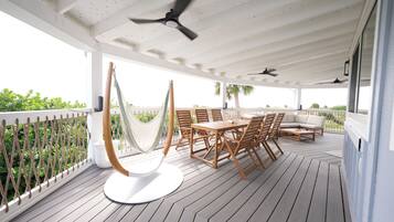 An outdoor patio with a wooden table and chairs, a hammock, and ceiling fans.