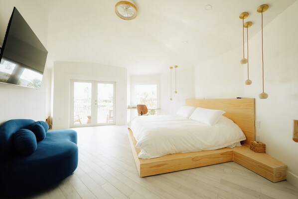 A bedroom with a bed, a blue chair, a TV, and a balcony.