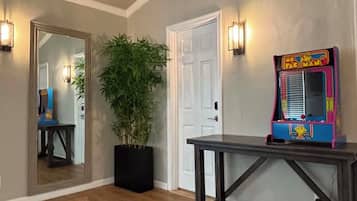 A room with a wooden floor, a potted plant, a table, and a colorful arcade machine.