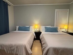 Hotellihuone, jossa on kaksi sänkyä, ja jokaisessa sängyssä on tyyny sekä yöpöytä, jossa on lamppu.