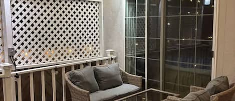 An outdoor patio area with wicker furniture, a glass table, and string lights.