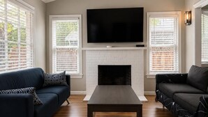 A living room with a fireplace, two sofas, a coffee table, and a TV mounted above the fireplace. - 3B house in Redwood City Walk to Caltrain with AC Parking near Stanford 1Gbps (Redwood City)