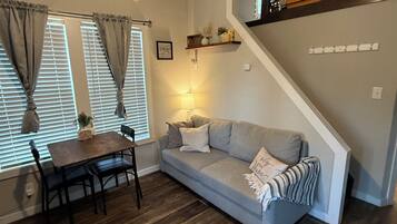 A living room with a sofa, a dining table with chairs, a ceiling fan, and a staircase.