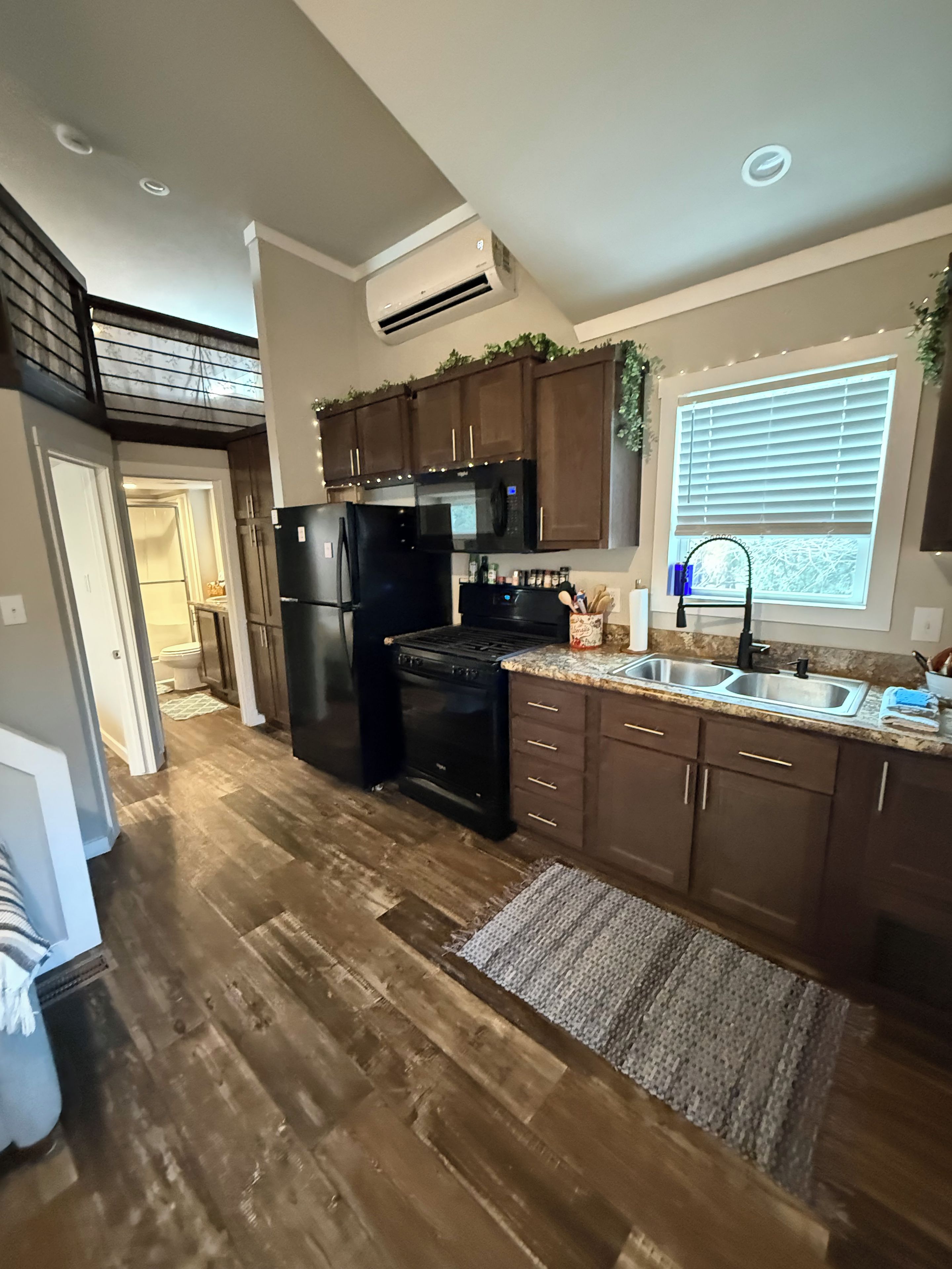 A modern kitchen with dark wooden cabinets, a black refrigerator, and a stainless steel sink.