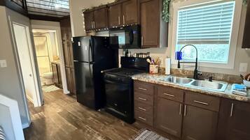 A modern kitchen with dark wooden cabinets, a black refrigerator, and a stainless steel sink.