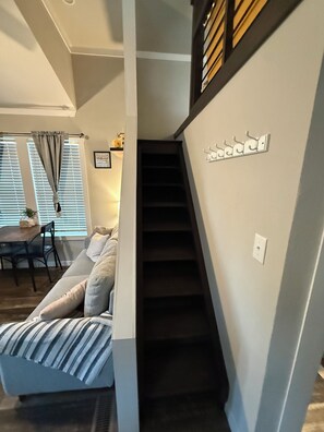 A staircase leading to a second floor, a sofa with striped cushions, a dining table with chairs, and a window with blinds. - This is an adorable tiny home that has unique charm. (Wheatland)