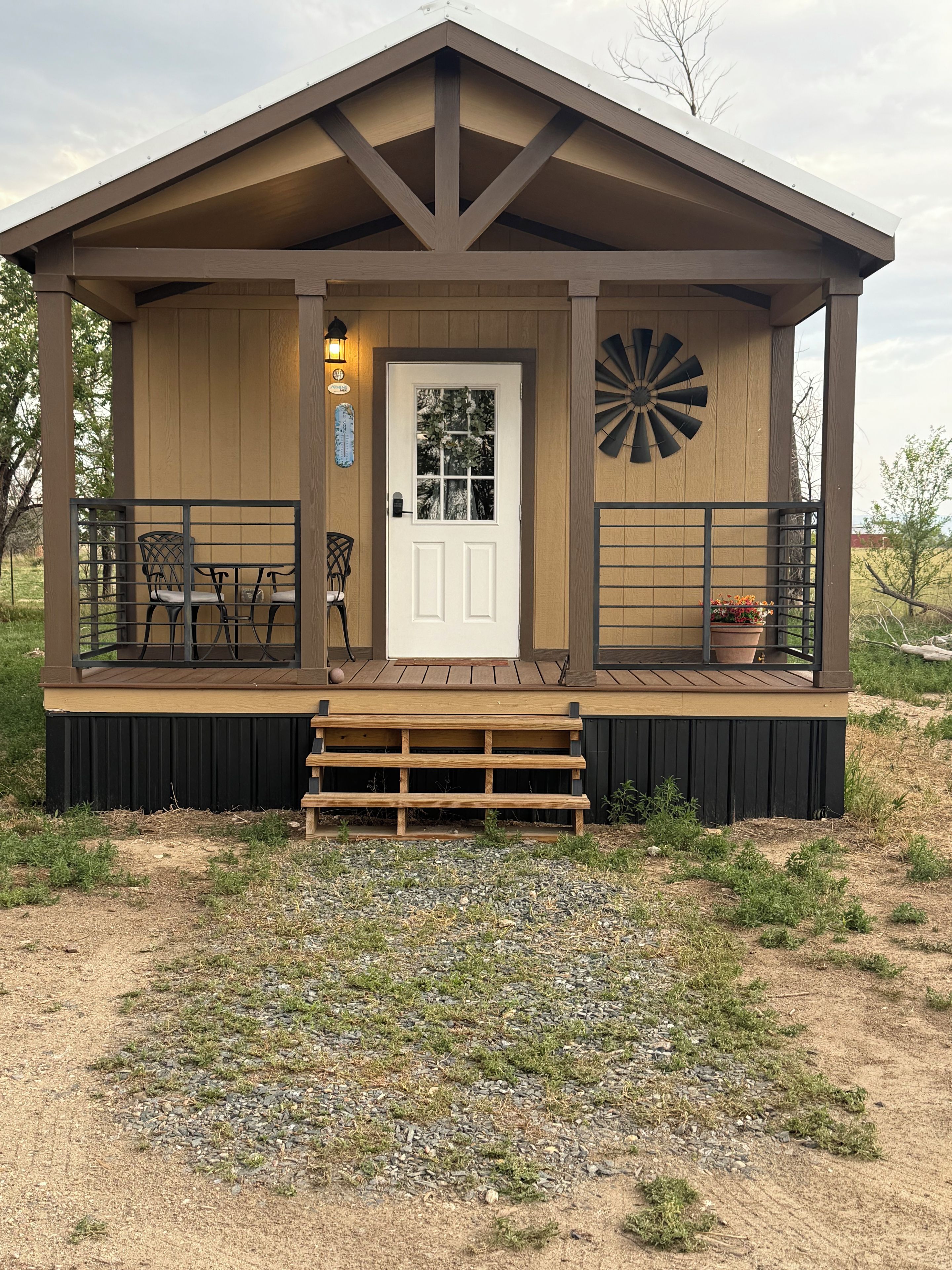 A wooden cabin with a front door, a small porch with a bench, and a windmill decoration.