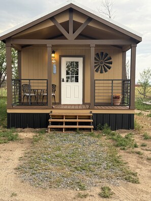 Una cabaña de madera con puerta principal, un pequeño porche con un banco y una decoración de molino.