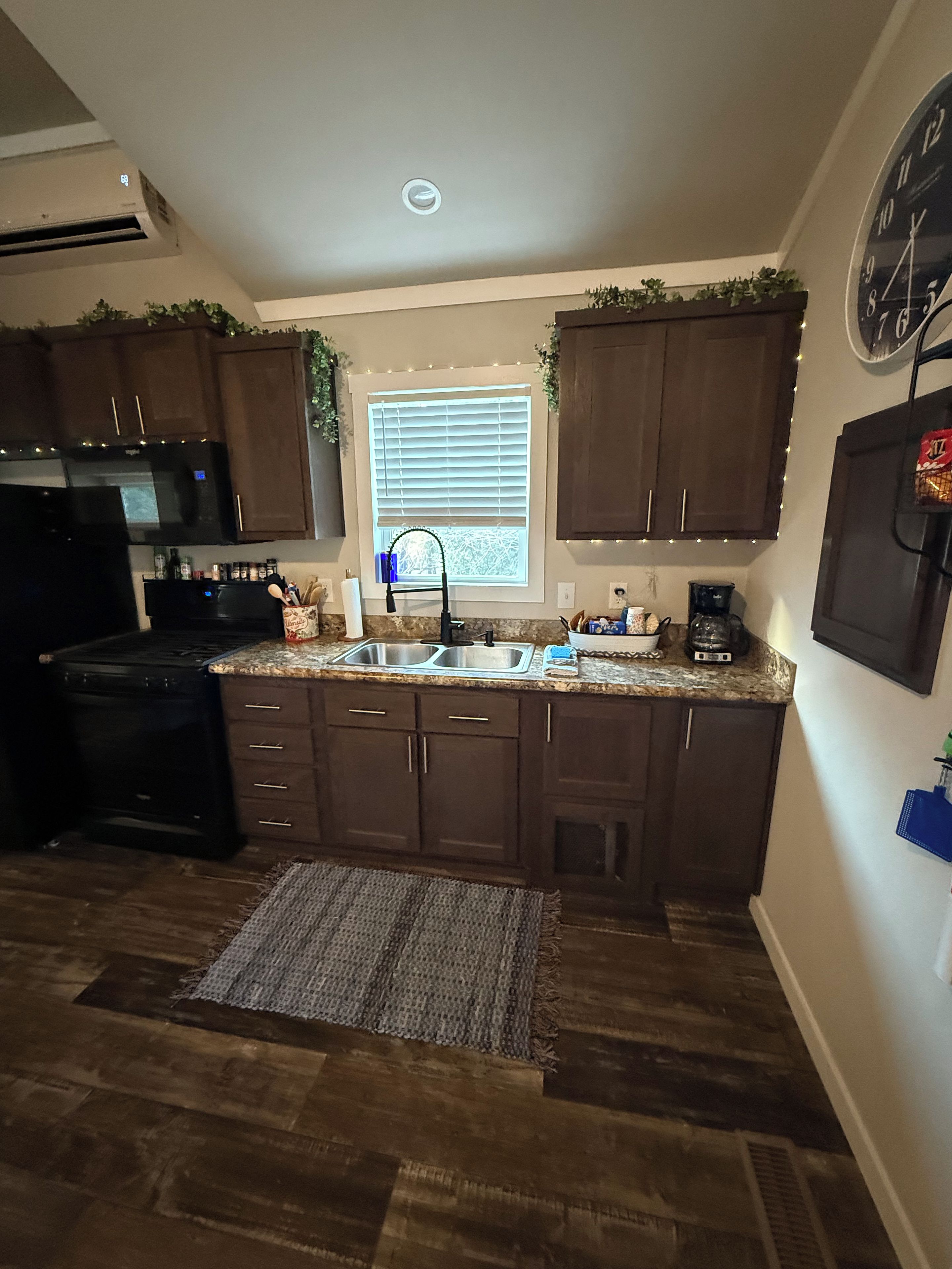 A kitchen with dark brown cabinets, a black stove, a double sink, and a window with blinds.